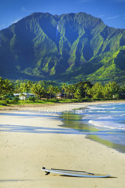 Vista de colocar a prancha de surf na praia de areia vazia com calma água azul do mar e colinas no fundo — Fotografia de Stock