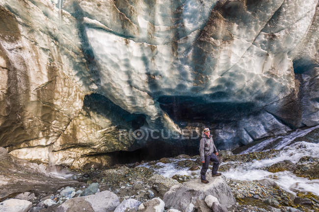 Чоловік стоїть на землі проти кам'янистої скелі і дивиться на камеру — стокове фото