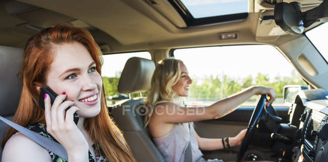 Two girls sitting in car while one driving another one speaking on cell phone — Stock Photo