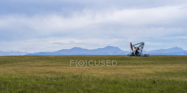 Derrick aceite trabajando en el campo con hierba verde y colinas en el fondo - foto de stock