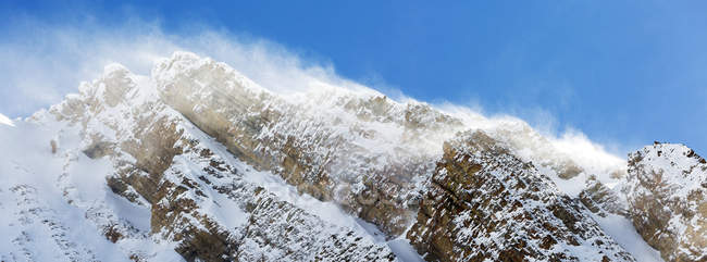 Gros plan d'un pic enneigé avec poudrerie et ciel bleu, parc provincial Peter Lougheed ; Alberta, Canada — Photo de stock