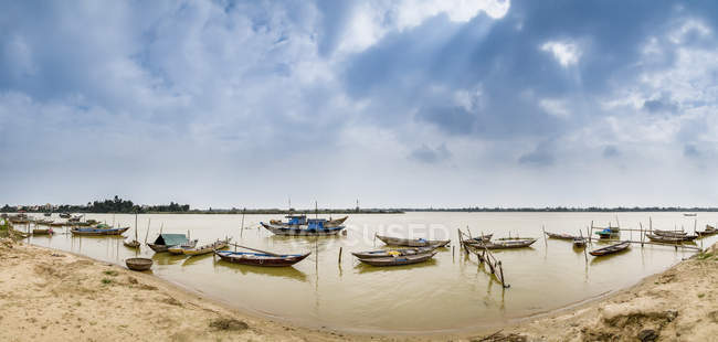 Barcos amarrados en aguas poco profundas a lo largo de la orilla; Thanh pho Hoi An, Quang Nam, Vietnam - foto de stock