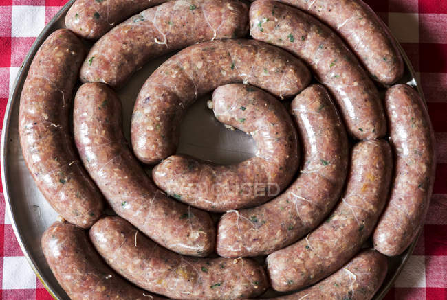 Close-up of a circle of uncooked sausage links on a round cooking tray on a red and white checkered tablecloth; Calgary, Alberta, Canada — Stock Photo