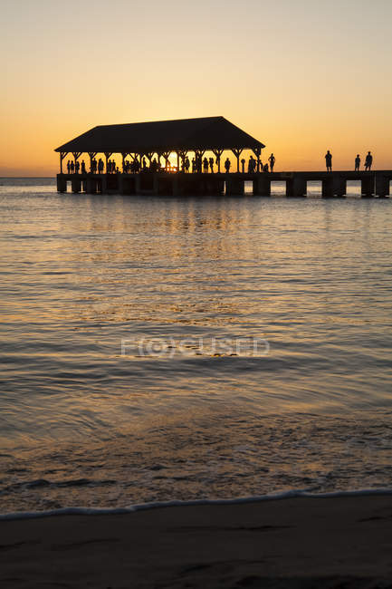 Sunset over ocean and silhouette of tourists on Hanalei Pier, Hanalei Bay; Hanalei, Kauai, Hawaii, United States of America — Stock Photo