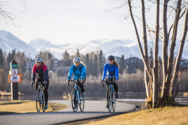 Three young women riding their bicycles on a trail along the water's edge; Anchorage, Alaska, United States of America — Stock Photo