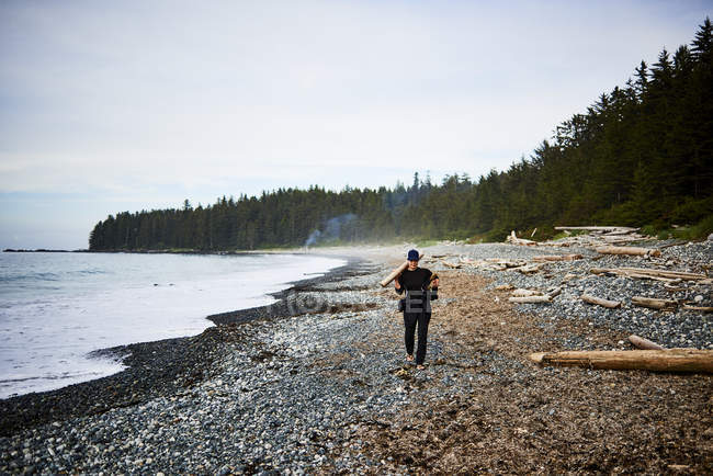 Frau läuft an einem felsigen Strand entlang und sammelt Feuerholz im cape scott provincial park, vancouver island, britisch columbia, canada — Stockfoto