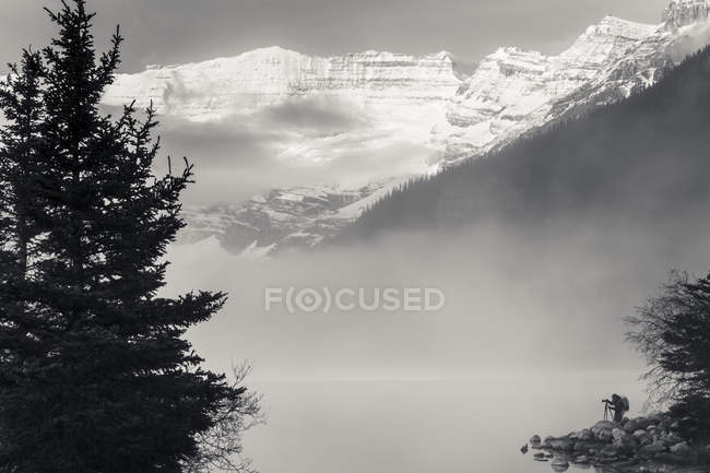 Silhouette di un fotografo sulla riva del lago Louise con nebbia che sorge dal lago all'alba, Banff National Park; Lake Louise, Alberta, Canada — Foto stock