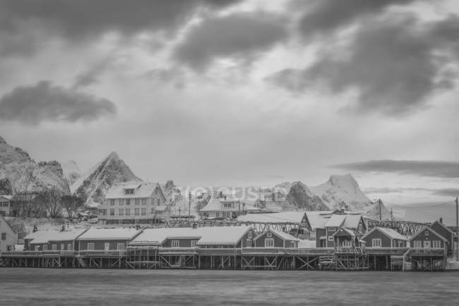 Häuser auf Stelzen am Ufer des Wassers mit schroffen Bergen im Hintergrund und Wolken; svolvar, erhabene Inseln, Norland, Norwegen — Stockfoto