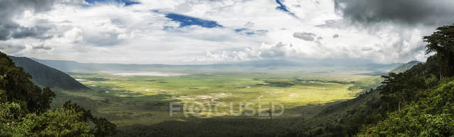 Nubes llenan el cielo y proyectan sombras en el verde valle rodeado de montañas; Tanzania - foto de stock