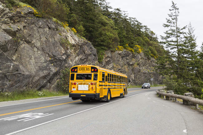A yellow school bus and car on a highway bridge over Deception Pass, Whidbey Island; Washington, United States of America — Stock Photo