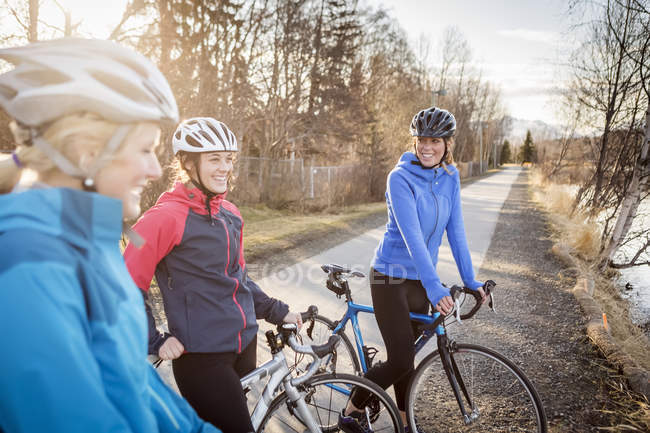 Three young women on their bicycles on a trail at sunrise; Anchorage, Alaska, United States of America — Stock Photo