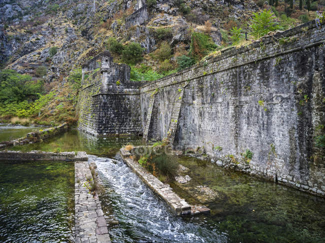 Un muro di pietra usurato con acqua a cascata lungo la baia di Kotor; Kotor, Montenegro — Foto stock
