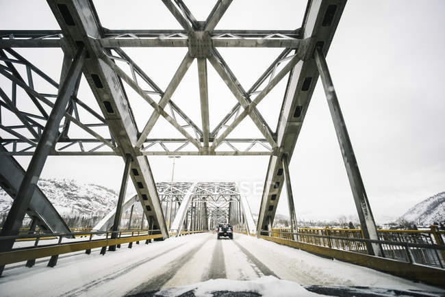Vehículos que viajan en una carretera cubierta de nieve sobre un puente con vistas desde la parte delantera de un vehículo; Nelson, Columbia Británica, Canadá - foto de stock