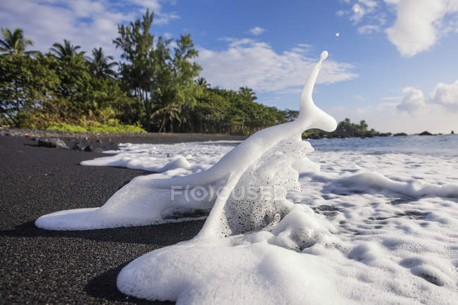Schiuma marina spruzzata sulla spiaggia di sabbia nera di Hana; Hana, Maui, Hawaii, Stati Uniti d'America — Foto stock