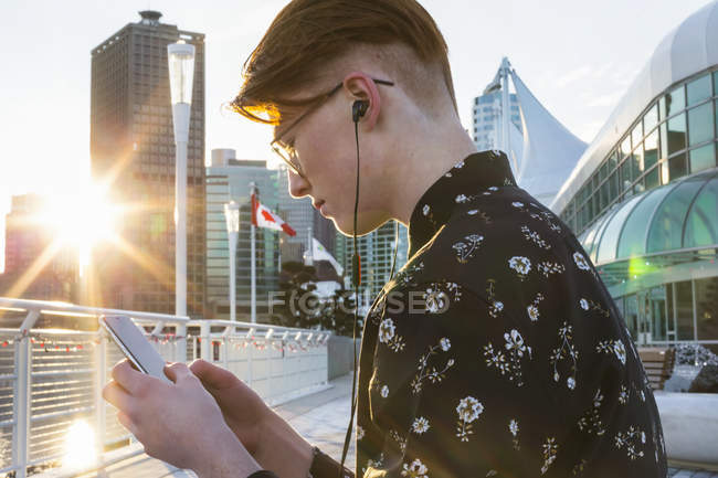 Ragazzo adolescente che usa il suo smartphone e indossa auricolari nel centro di Vancouver; Vancouver, Columbia Britannica, Canada — Foto stock