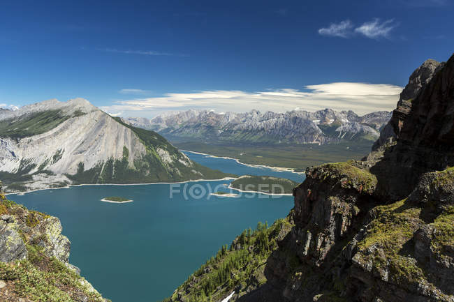 View from the top of mountain ridge looking down on colourful alpine lake and mountain range in the distance with blue sky and clouds; Kananaskis Country, Alberta, Canada — Stock Photo