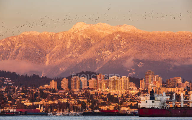 El horizonte de Vancouver del Norte y las Montañas Costeras brillando al atardecer y barcos en el puerto; Vancouver, Columbia Británica, Canadá - foto de stock