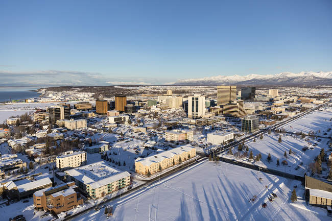 Вид с воздуха на снежный покров в центре Анкориджа и горы Чугач и Талкитна, простирающийся вдалеке за городом, Парк Сектор виден на переднем плане, Юго-Центральная Аляска зимой; Анкоридж, Аляска — стоковое фото