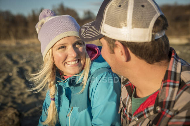 Una pareja joven se sienta a hablar en una playa al atardecer; Anchorage, Alaska, Estados Unidos de América - foto de stock