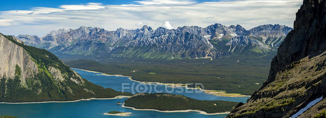 Panorama au sommet de la crête montagneuse regardant vers le bas sur le lac alpin coloré et la chaîne de montagnes au loin avec ciel bleu et nuages ; Kananaskis Country, Alberta, Canada — Photo de stock