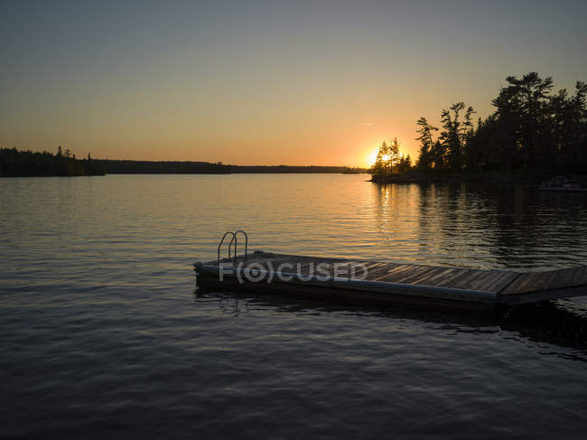 The sun setting over Lake of the Woods with a dock in the foreground; Lake of the Woods, Ontario, Canada — Stock Photo