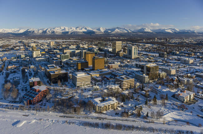 Vue aérienne de la neige recouvrant le centre-ville d'Anchorage et les montagnes Chugach au loin, les bâtiments Capitan Cook Hotel et Conoco Philips au premier plan, le centre-sud de l'Alaska en hiver ; Anchorage, Alaska, États-Unis d'Amérique — Photo de stock