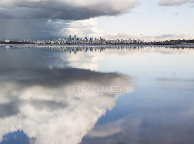 Distant view of the Vancouver skyline over the Pacific Ocean reflecting clouds, viewed from Spanish Banks; Vancouver, British Columbia, Canada — Stock Photo