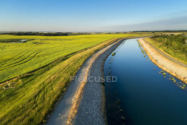 Um canal de irrigação com um caminho que corre ao seu lado e céu azul, a leste de Calgary; Alberta, Canadá — Fotografia de Stock