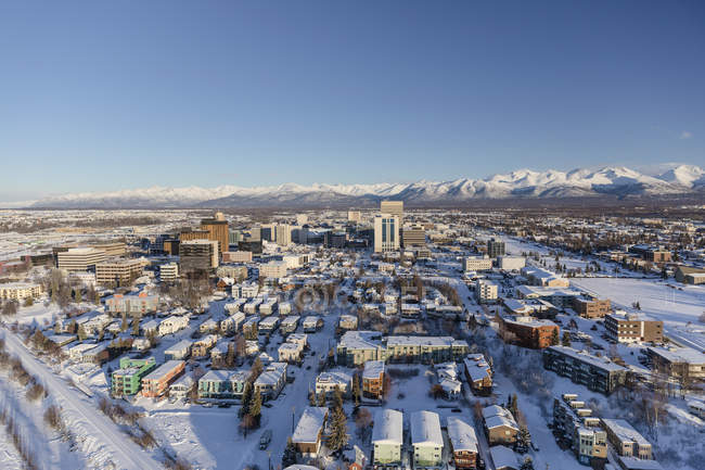 Vue aérienne de la neige recouvrant le centre-ville d'Anchorage et les montagnes Chugach au loin, le Park Strip et le Capitan Cook Hotel visibles au premier plan, au centre-sud de l'Alaska en hiver ; Anchorage, Alaska, États-Unis d'Amérique — Photo de stock