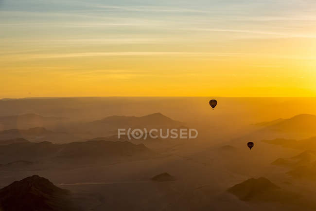 Silueta de globos de aire caliente en el cielo dorado sobre las dunas de arena al amanecer en el desierto de Namib; Sossusvlei, región de Hardap, Namibia - foto de stock