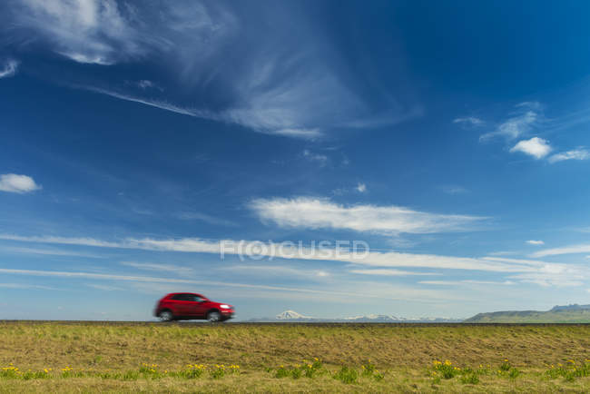 Red car driving on open road near Hella with Hekla volcano in the distance; Iceland — Stock Photo