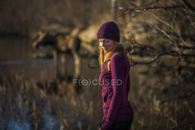 Im Vordergrund steht eine junge Frau mit einem Kuh-Elch (alces alces) im Teich im Hintergrund; Ankerplatz, alaska, vereinigte Staaten von Amerika — Stockfoto