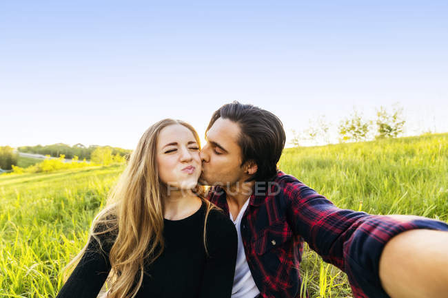 Jeune couple assis dans un champ et prendre un selfie — Photo de stock
