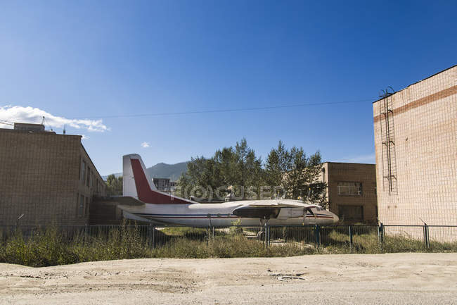 Un viejo avión abandonado estacionado entre edificios y detrás de una valla; Ulán Bator, Ulán Battar, Mongolia - foto de stock