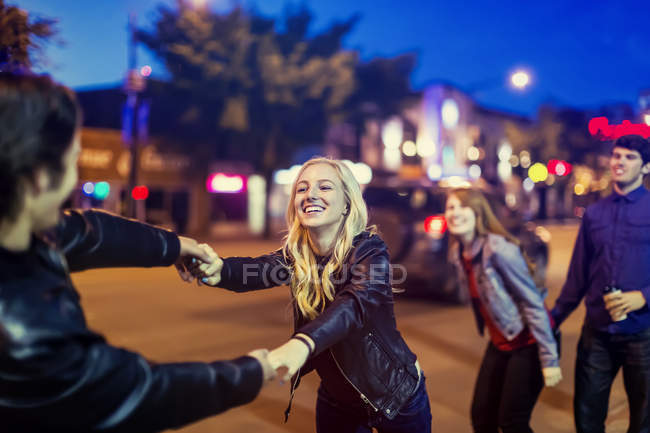 Two young couples being playful on the sidewalk beside a city street at dusk — Stock Photo