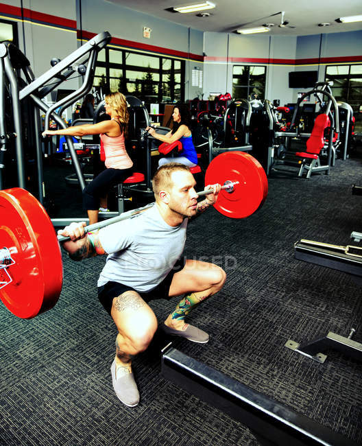 Молодой человек делает приседания подъемников во время его веса сопротивления тренировки в фитнес-центр — стоковое фото