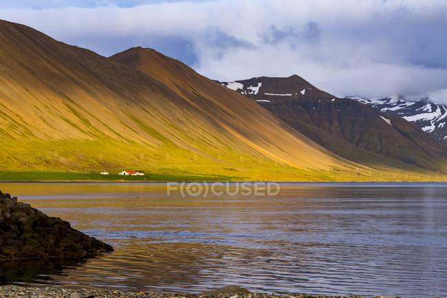 Ladera de colores vibrantes se ve reforzada por el sol poniente y los colores se reflejan en la bahía del océano en Islandia occidental, Islandia - foto de stock