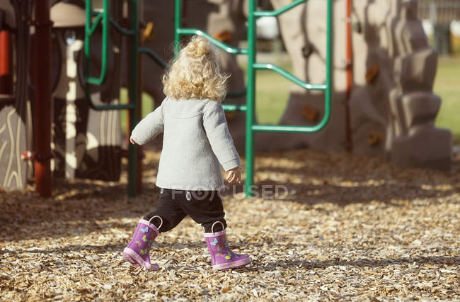 Mignonne jeune fille marchant dans une aire de jeux en bottes en caoutchouc — Photo de stock