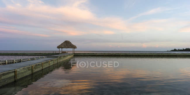 Banco en un muelle frente a la costa y mar abierto al amanecer, Belice - foto de stock