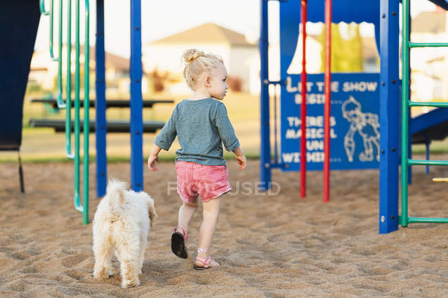 Rear view of young girl and pet dog playing in a playground — Stock Photo