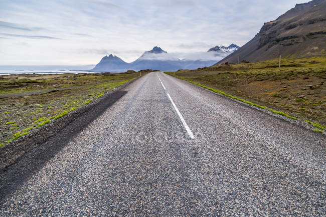 A longa estrada pavimentada que leva à paisagem montanhosa vulcânica à distância, Islândia — Fotografia de Stock