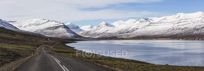 A estrada que corre ao longo de um fiorde na região do fiorde oriental da Islândia vista em direcção às montanhas; Islândia — Fotografia de Stock