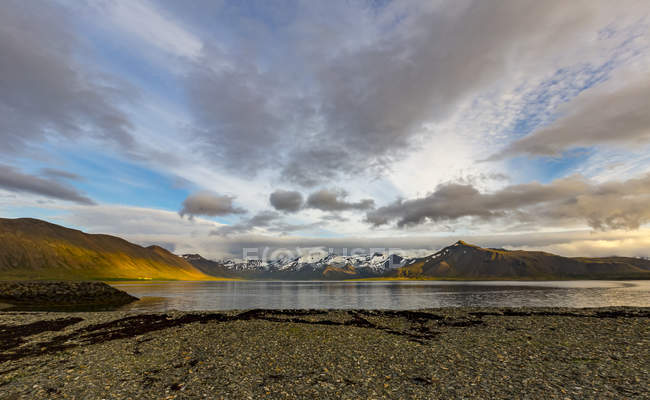 Los ricos colores de las colinas son vibrantes en la puesta de sol con el reflejo del océano en el oeste de Islandia - foto de stock