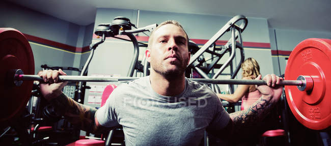 Un joven haciendo levantamientos en cuclillas durante su entrenamiento de resistencia al peso en un gimnasio - foto de stock