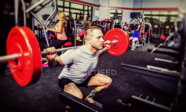 A young man doing squat lifts during his weight resistance training at a fitness facility — Stock Photo