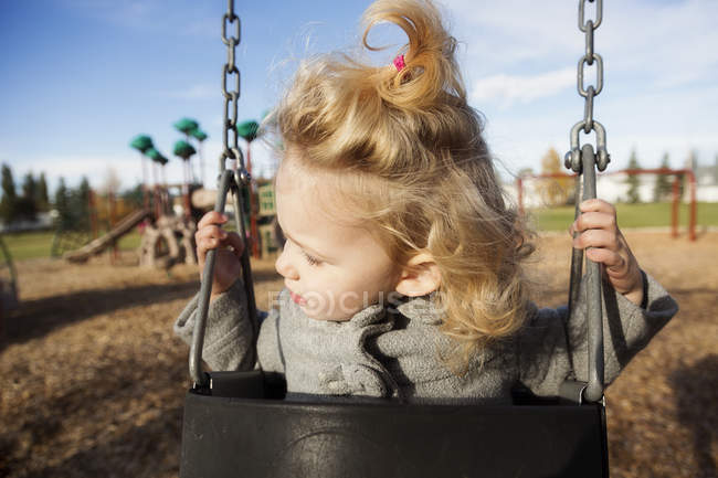 Cute young girl with funny face while swinging in a playground — Stock Photo