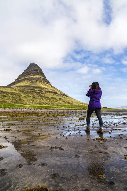 Rear view of female hiker taking photo with camera in front of Kirkjufell Mountain, Iceland — Stock Photo