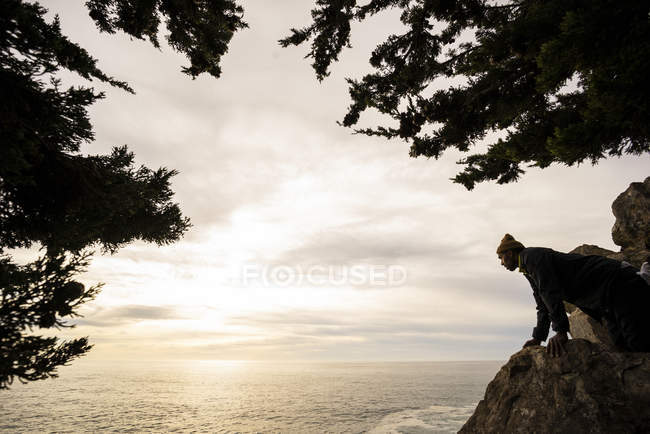 Man looking down over a rock to the ocean below at dusk — Stock Photo
