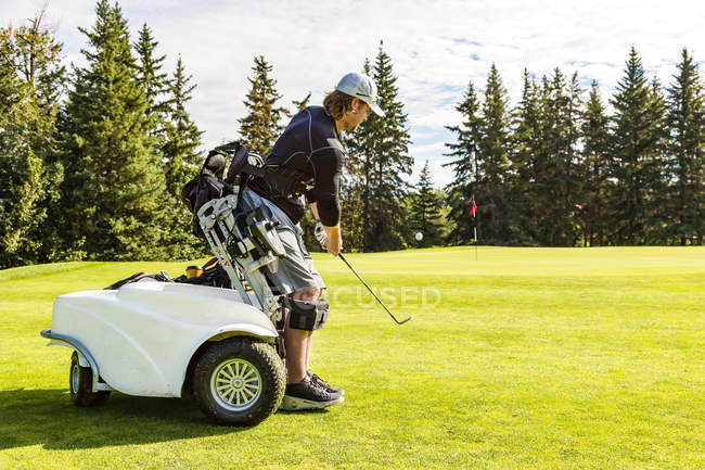 A physically disabled golfer chipping a ball onto the green and using a specialized golf assistance motorized hydraulic wheelchair, Edmonton, Alberta, Canada — Stock Photo