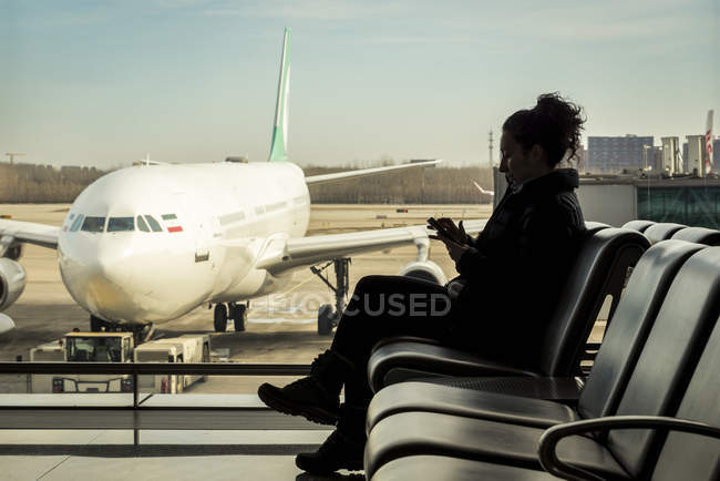 Passenger sitting in airport terminal using her smart phone, Beijing Capital International Airport, Beijing, China — Stock Photo